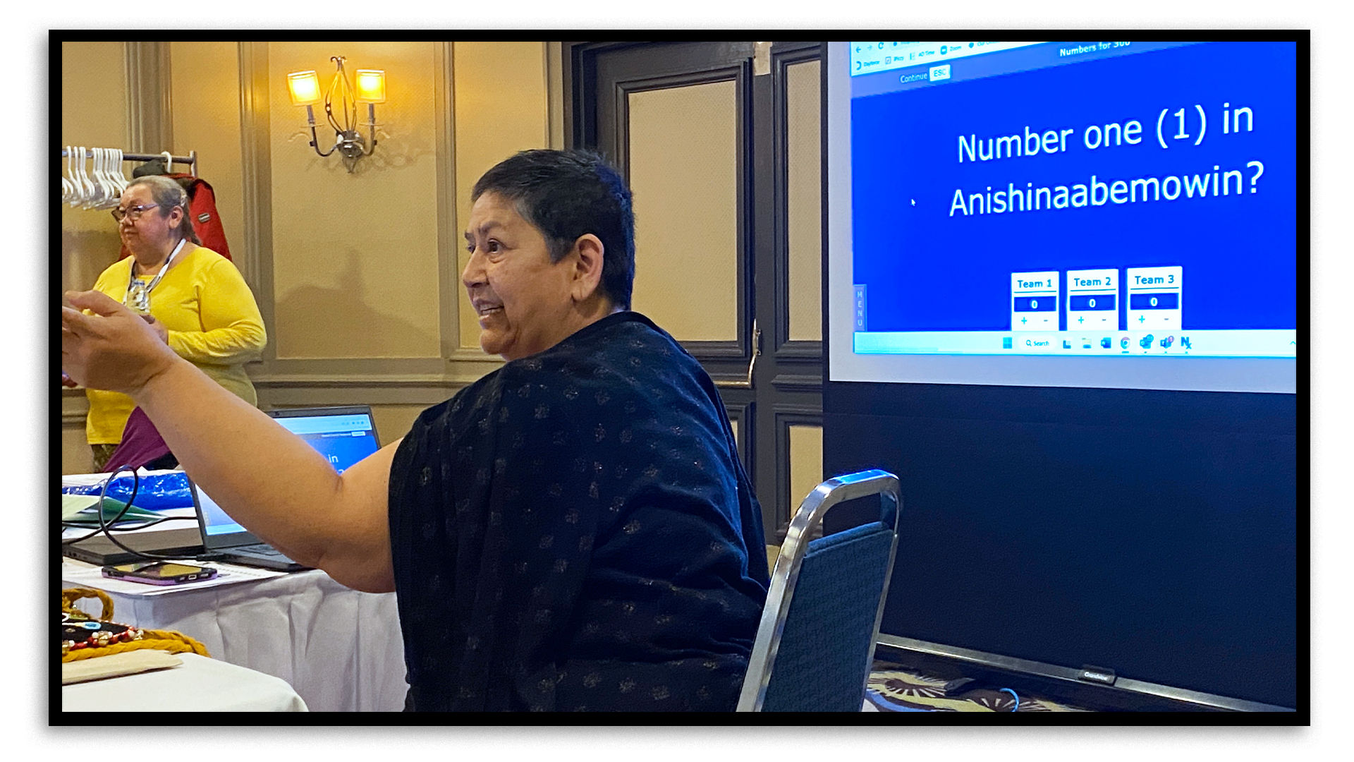 In a hotel’s conference room in Sudbury, two women animate a game of Jeopardy! There’s a projector screen behind them and the question “Number one in Anishinaabemowin?” is on the screen. At the bottom of the screen, the points scored so far by each of the three teams competing in the game are on display.