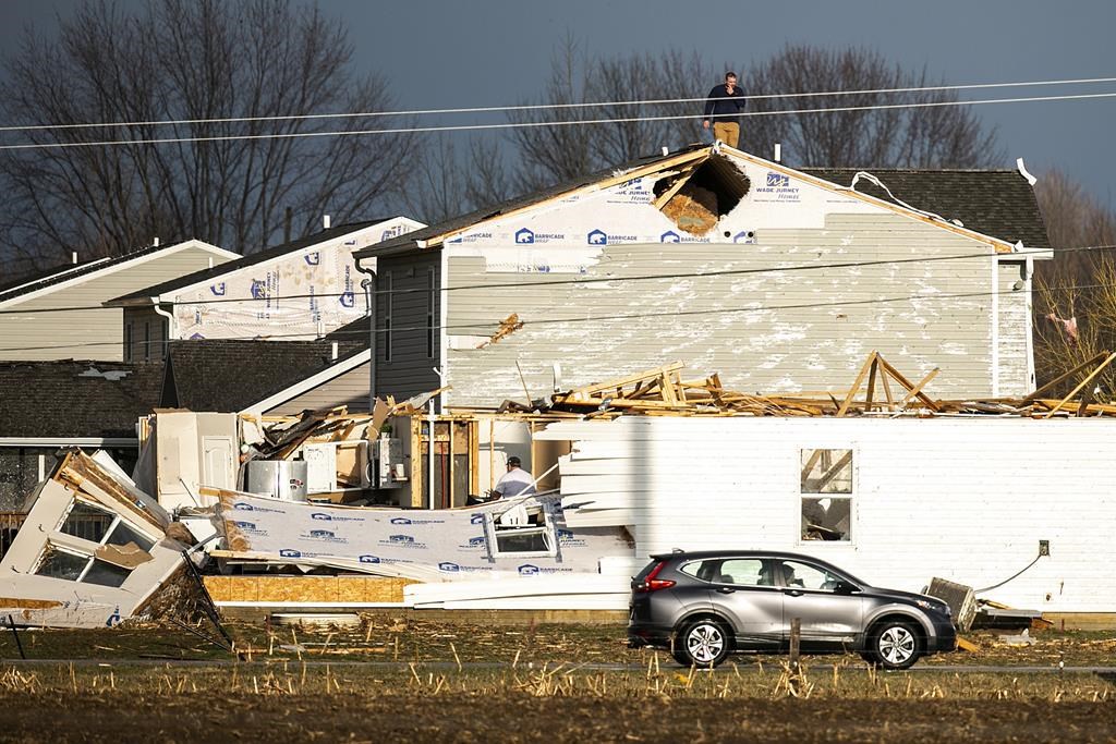 A person walks on the roof of a building damaged in a storm after a tornado warning in Johnson County, Friday, March 31, 2023, in Hills, Iowa.