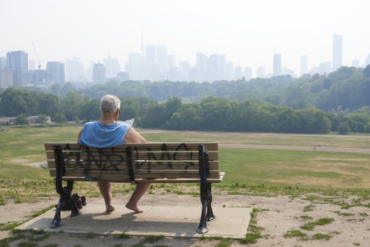A person sits on a bench overlooking Riverdale Park East in Toronto on June 6, 2023, as the city remains under a special air quality statement caused by forest fires.