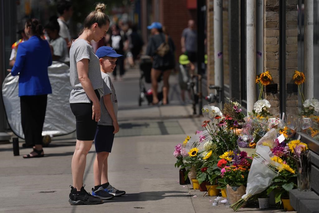 Passers-by stop to look at a makeshift memorial at the place where a mother of two, Karolina Huebner-Makurat was killed by a stray bullet and the accused has been charged with second degree murder.