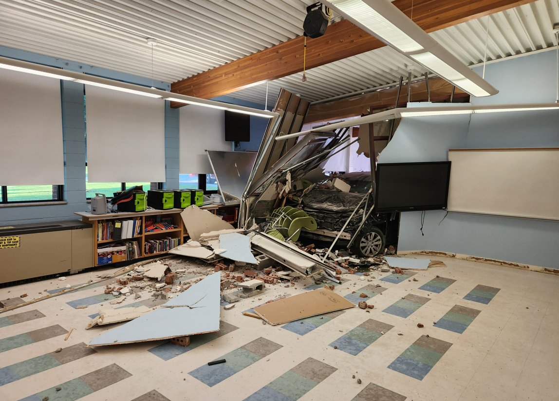 A vehicle partially through a wall in an empty classroom.