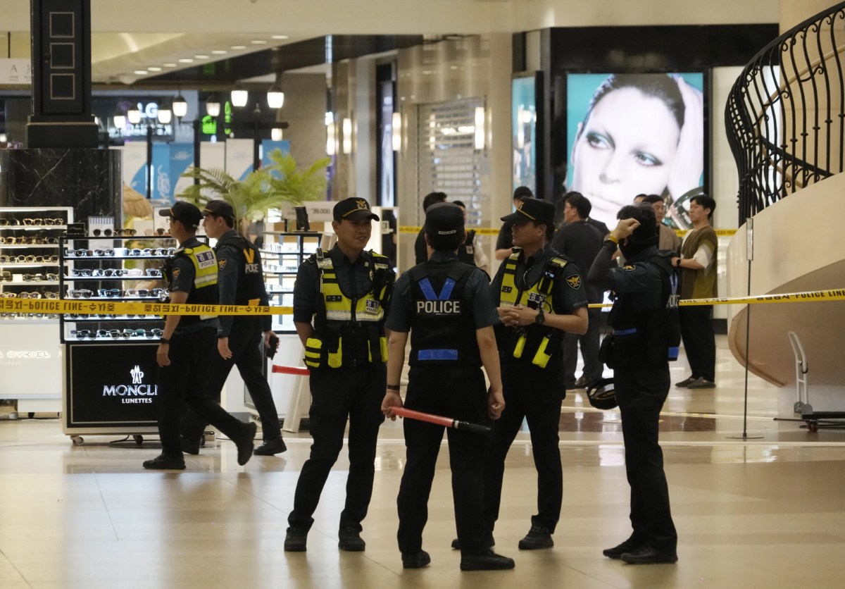 Police stand in a circle. There is yellow crime scene tape behind them.