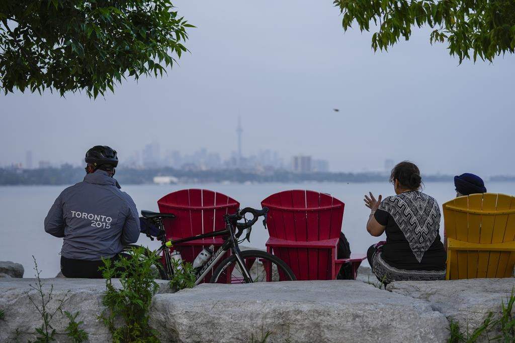People sit along the waterfront at Humber Bay Park in Toronto, on Wednesday, June 28, 2023. 