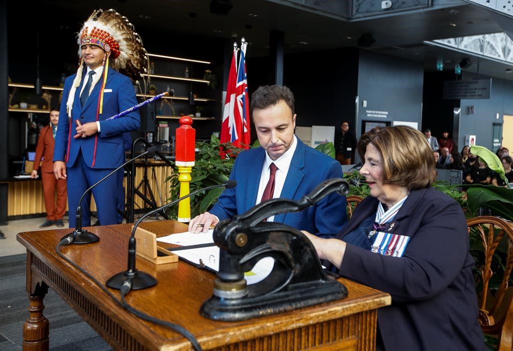 Manitoba Premier Wab Kinew looks on as Adrien Sala, minister of finance, is sworn-in by Lt. Gov. Anita Neville in Winnipeg on Wednesday, Oct. 18, 2023. Manitoba's new NDP government may push back a promise to freeze hydroelectric rates for one year. New numbers from Crown-owned Manitoba Hydro show the utility is now expecting a net loss this year instead of the profit it predicted in the spring. 