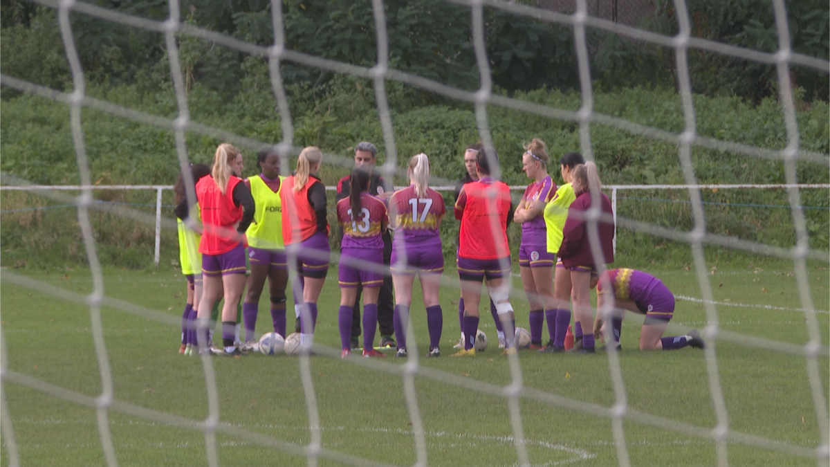 A group of female soccer players at Clapton Community FC, weaing a purple, yellow and red kit form a circle before a game in London, England on November 5, 2023.