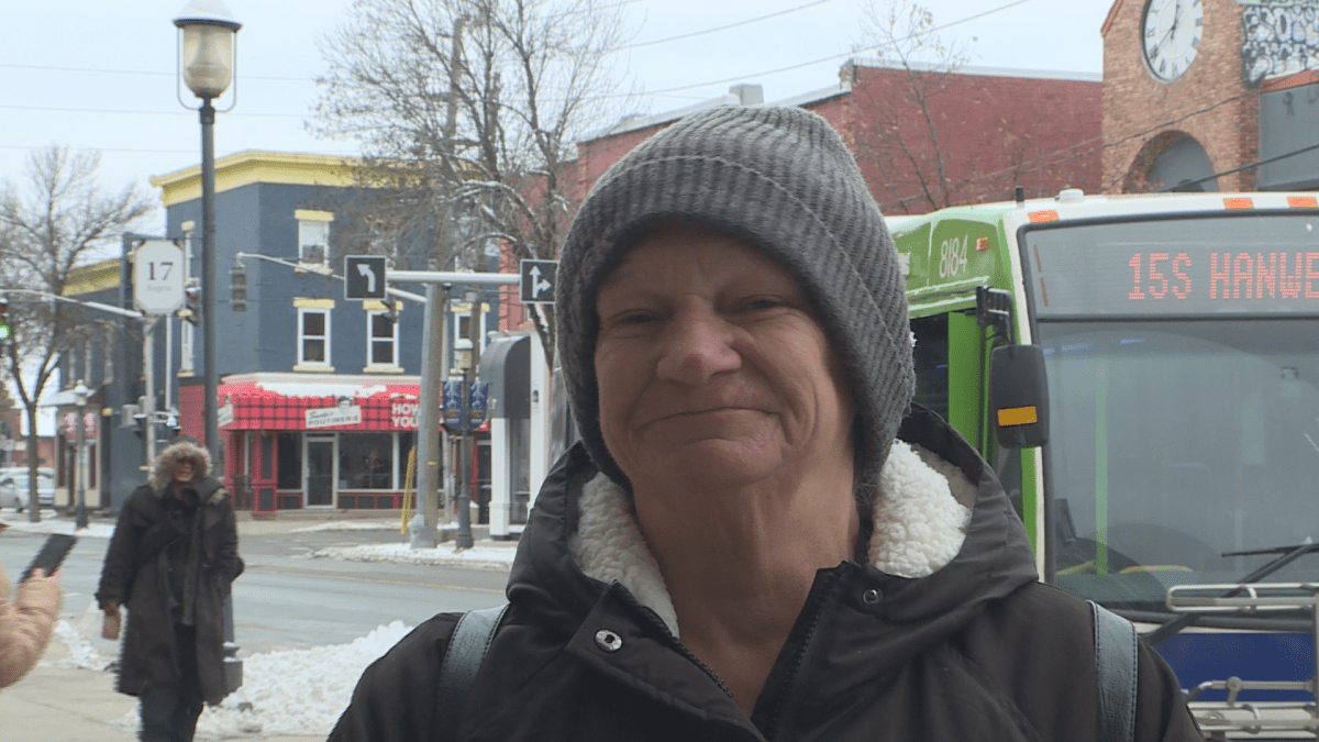 A woman standing in front of a road with a bus behind her.