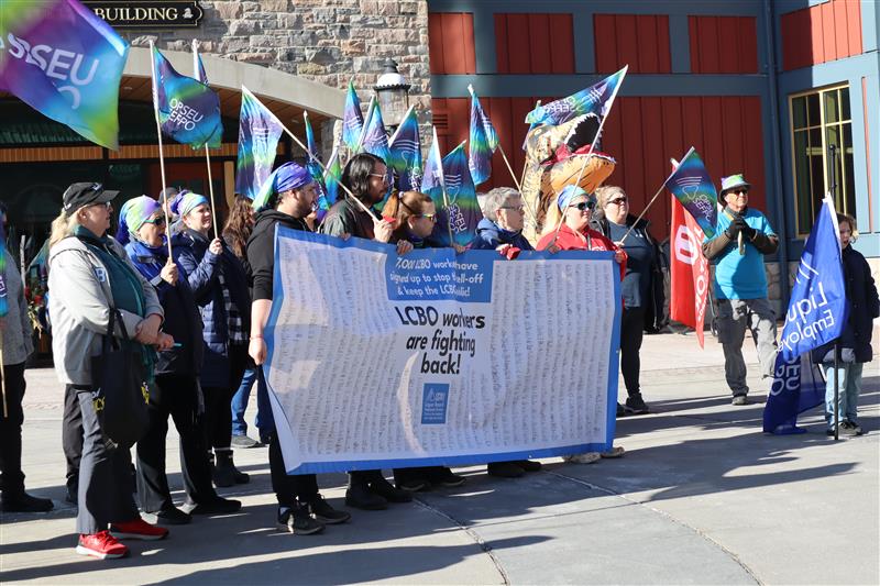 People waving flags and holding a large banner in front of an old building.