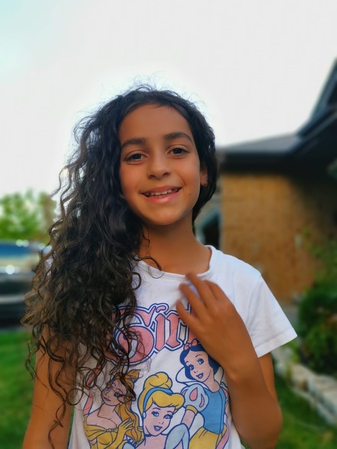 A picture of a girl with brown hair and a t-shirt outside in warm weather.