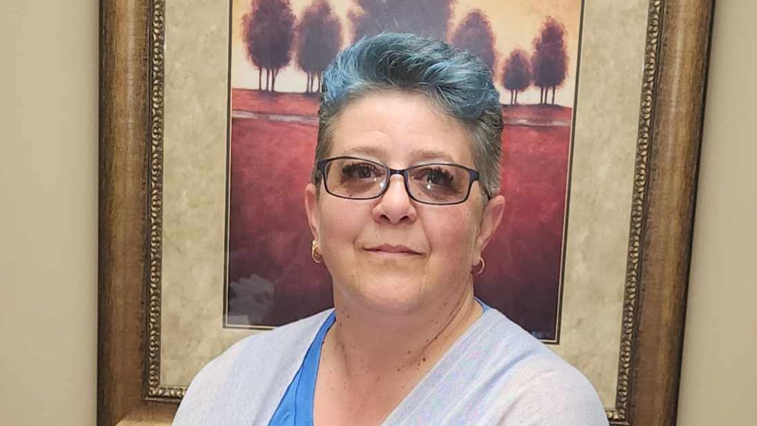 A woman with blue hair and glasses poses for a portrait.