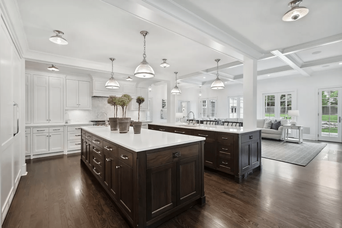 The kitchen. It is white and there are two dark wood islands in the centre.