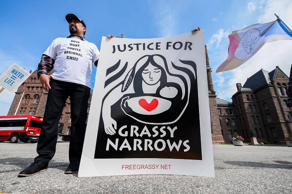A demonstrator holds a sign following a press conference announcing intention to litigate against the Government over contamination of Grassy Narrows, in Toronto on June 4, 2024. THE CANADIAN PRESS/Christopher Katsarov.