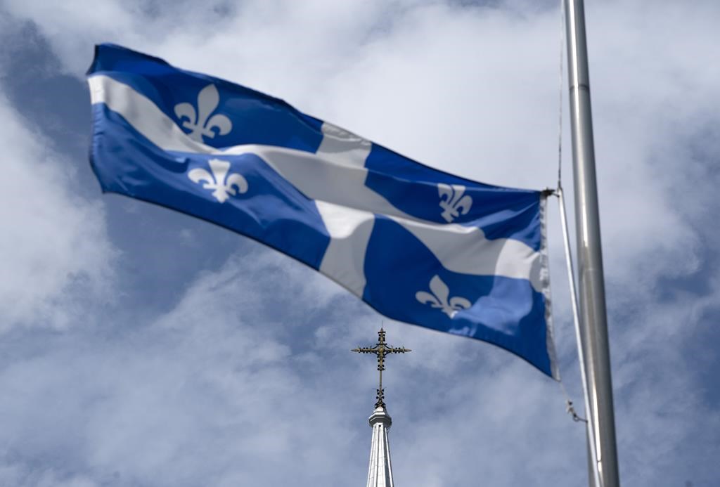 The Quebec flag flies on a flag pole near a church.