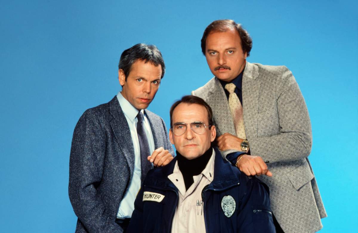 Three men pose for a photo in costume. Sikking sits in the middle, stone faced.