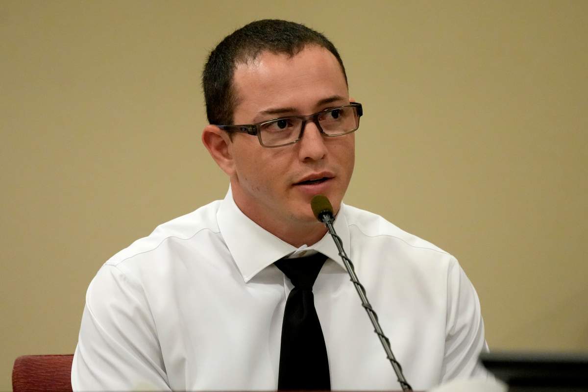 Nicholas LeFleur in a white shirt and black tie. He sits in front of a microphone.