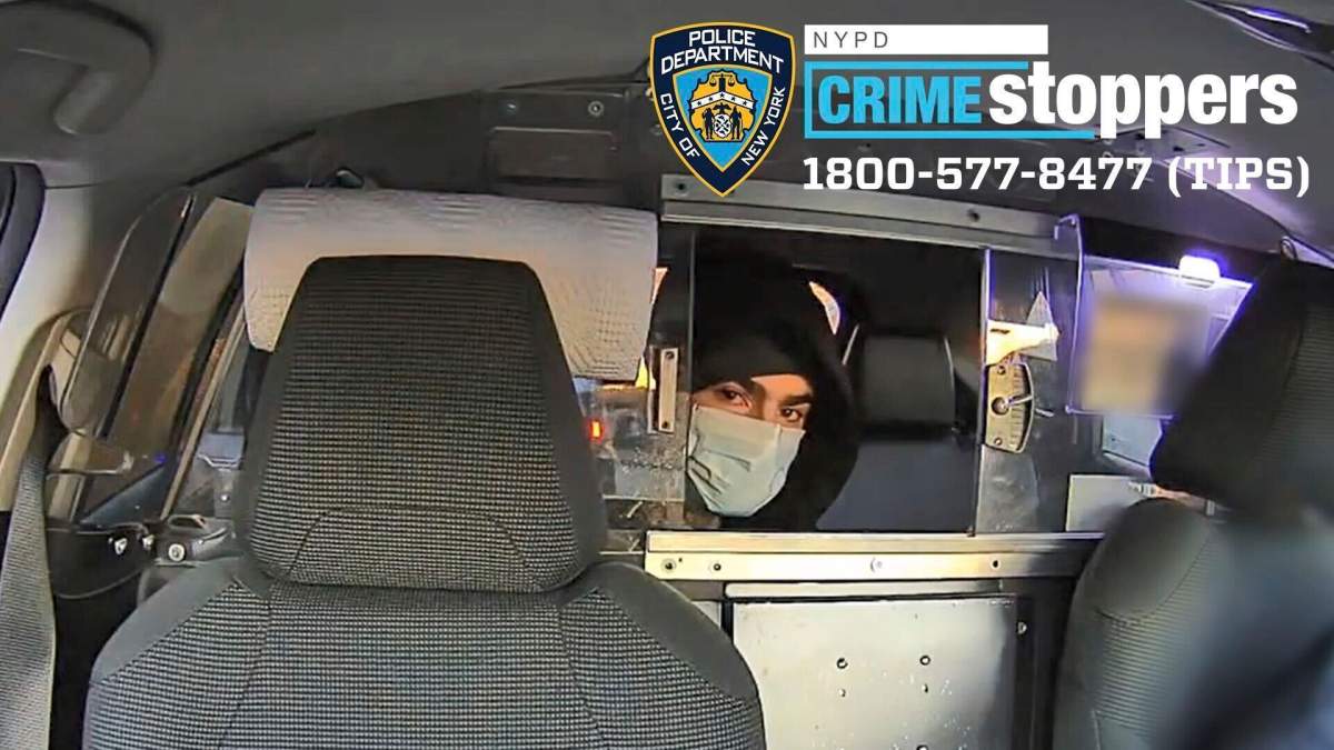 A man in a hoodie and face mask peers through the window of a vehicle.