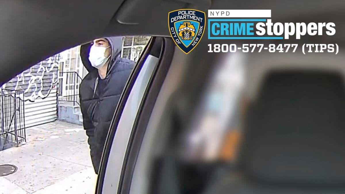 A man in a hoodie and face mask walks past the open door of a vehicle.