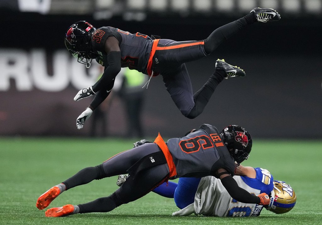 B.C. Lions' Emmanuel Rugamba (33) leaps over T.J. Lee (6) to avoid colliding with him as he tackles Winnipeg Blue Bombers' Nic Demski, bottom, during the first half of CFL football game in Vancouver, on Saturday, Oct. 15, 2022. Rugamba embraces the challenge of helping return the Edmonton Elks to the CFL playoffs.