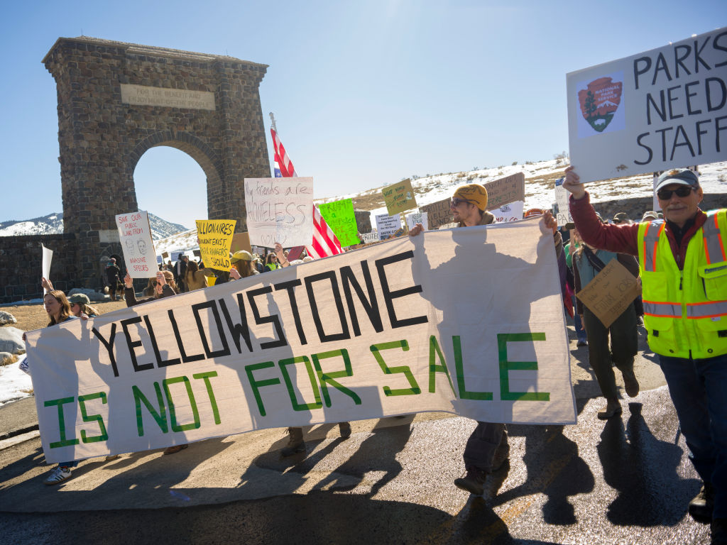 Protesters hold signs at Roosevelt Arch, the northern entrance to Yellowstone Park on March 1, 2025 in Gardiner, Montana.