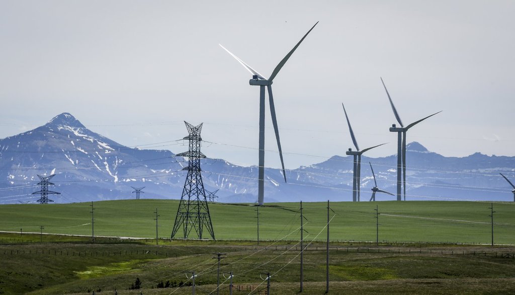 Power transmission lines and wind turbines as seen with the Rocky Mountains in the background near Pincher Creek, Alta., Thursday, June 6, 2024.