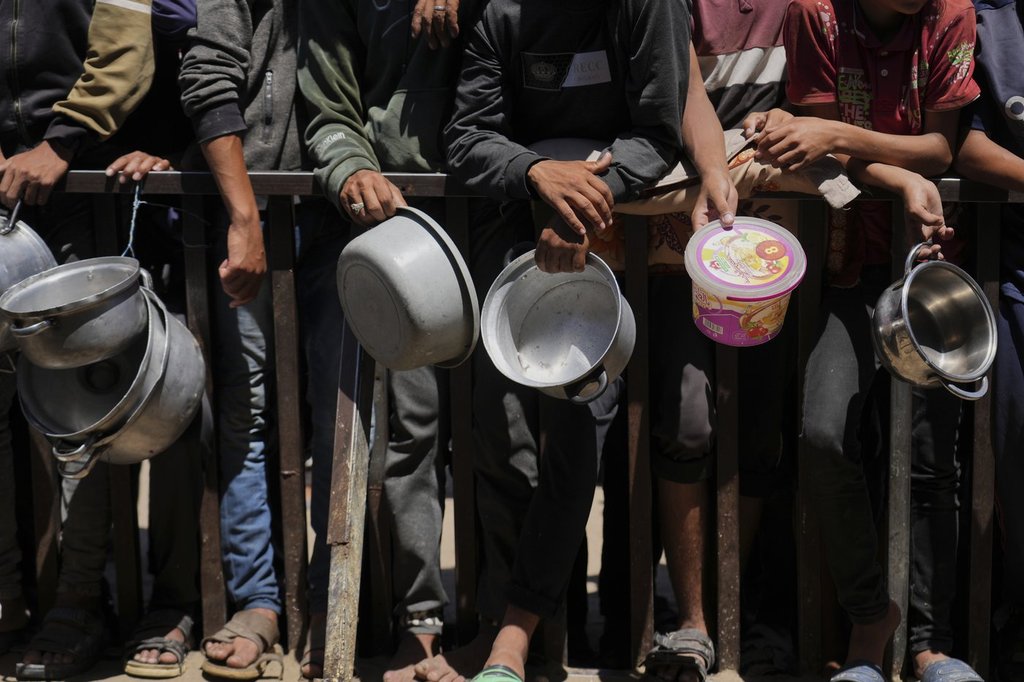 Holding their pots, Palestinians wait to get donated food at a community kitchen in Khan Younis, southern Gaza Strip, Monday, June 2, 2025.