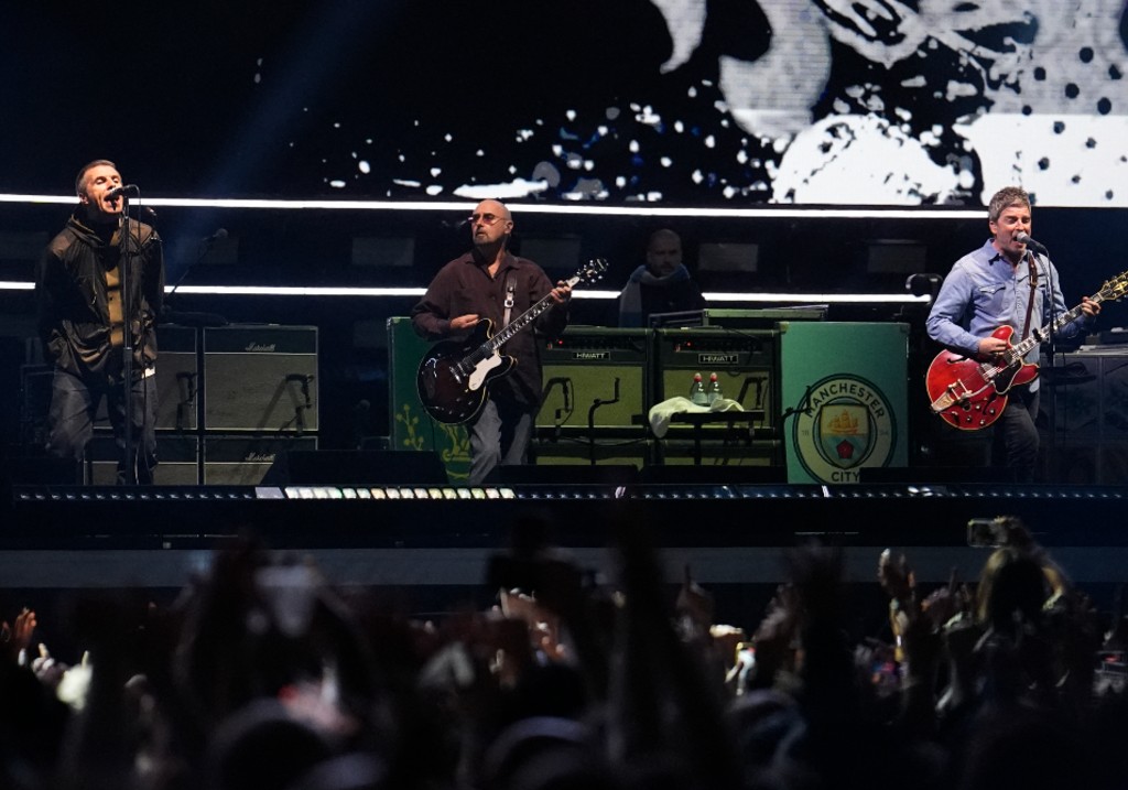 (L-R) Liam Gallagher, lead singer, Paul Arthurs, guitarist and Noel Gallagher, singer and guitarist of British rock band Oasis perform on stage at the Principality Stadium in Cardiff on July 4, 2025.
