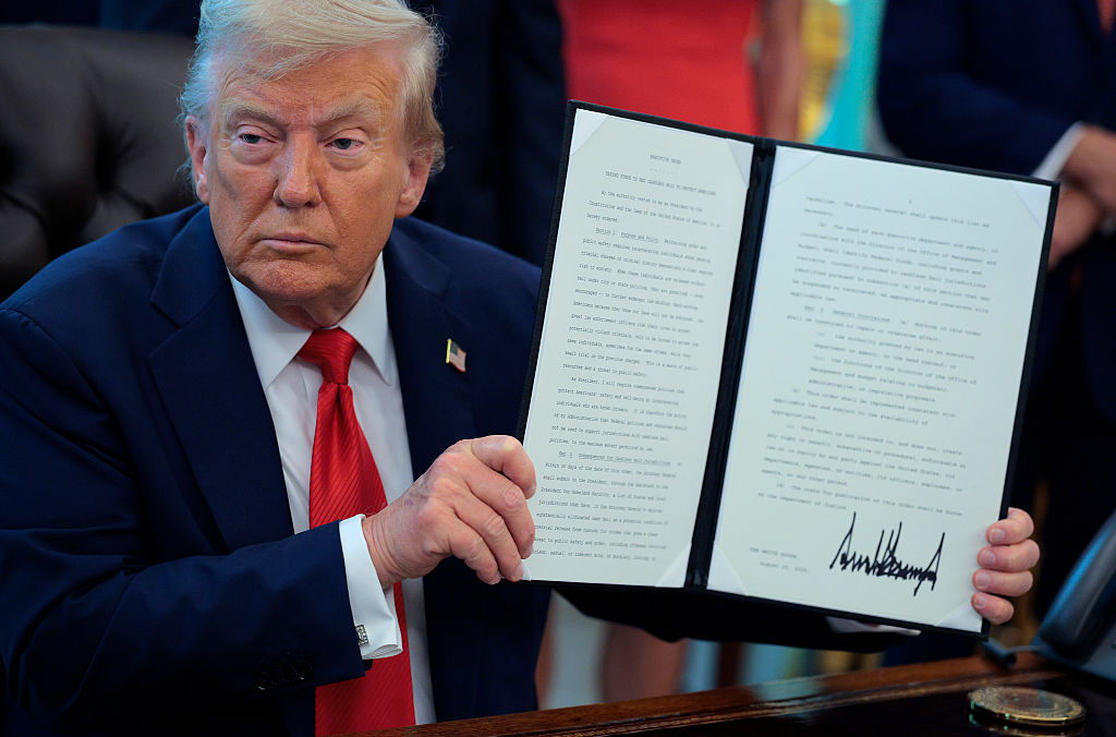 U.S. President Donald Trump signs executive orders in the Oval Office at the White House on August 25, 2025 in Washington, DC. Furthering his federal takeover of the capital city’s law enforcement, Trump signed orders ending cashless bail in the District of Columbia, mandating prosecution for people who desecrate the American flag -- including by burning it -- and other orders.