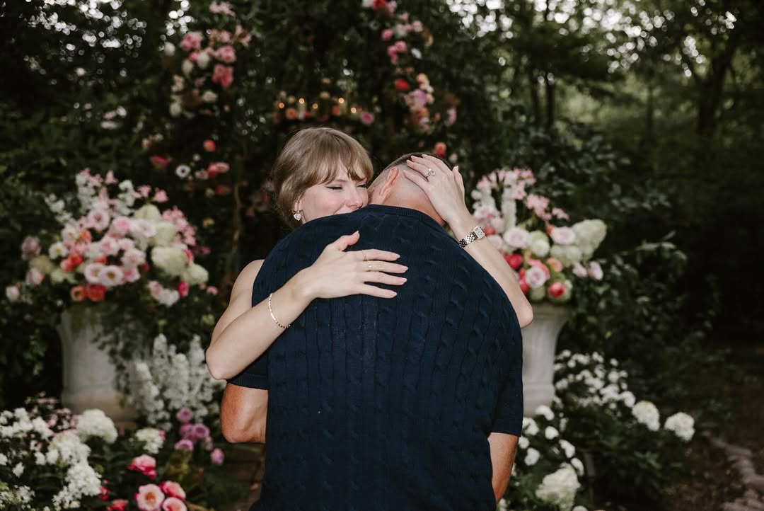 The next picture in the slide show is of the couple hugging, with Kelce’s back to the camera. Swift’s right hand, with her new engagement ring and watch on full display, rests gently on the back of Kelce’s head. Her left arm, resting on Kelce’s back, sports a thin golden bracelet.