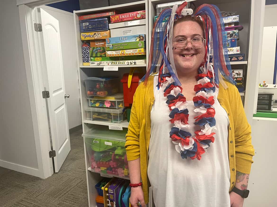 A woman wearing accessories in Acadian colours smiles in front of shelves full of board games.