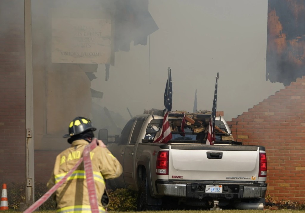 A vehicle that was rammed into the building is surrounded by smoke as a firefighter works on the scene at the Church of Jesus Christ of Latter-day Saints in Grand Blanc, Mich., Sunday, Sept. 28, 2025.