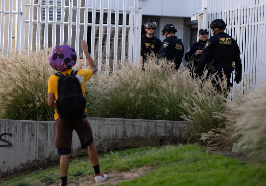 A protester waves to Department of Homeland Security officials as they walk to the gates of the U.S. Immigration and Customs Enforcement facility after inspecting an area outside on Sunday, Sept. 28, 2025, in Portland, Ore.