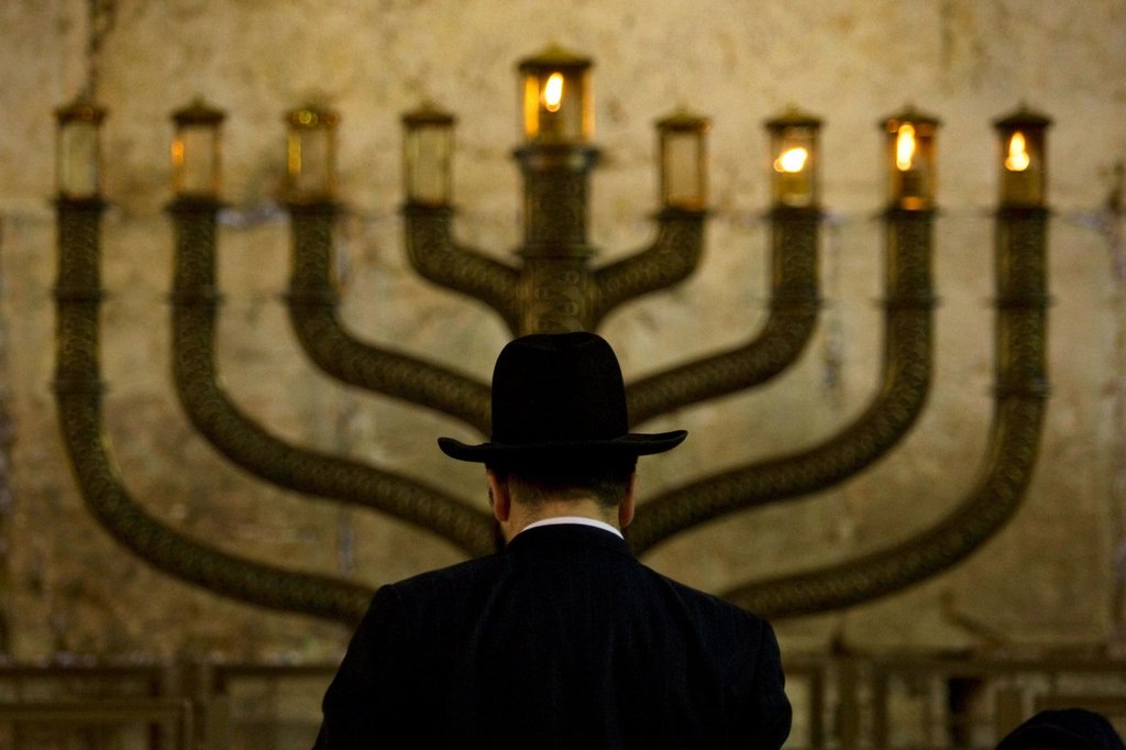 FILE - An Ultra-Orthodox Jewish man stands in front of a menorah on the third eve of Hanukkah, at the Western Wall, Judaism's holiest site in Jerusalem's old city, Sunday, Dec. 13, 2009. (AP Photo/Sebastian Scheiner, File).
