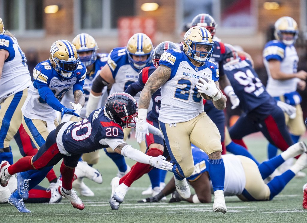 Winnipeg Blue Bombers' Brady Oliveira (20) runs with the ball while defended by Montreal Alouettes' Lorenzo Burns (20) during second half Eastern semi-final action, in Montreal on Saturday, Nov. 1, 2025. THE CANADIAN PRESS/Christopher Katsarov.
