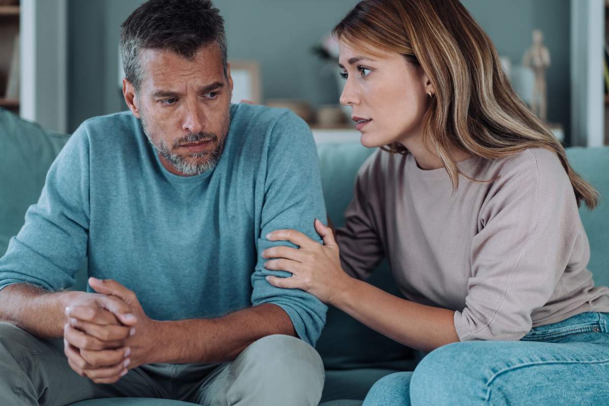A man is comforted by his partner after receiving a denial letter from his insurer.