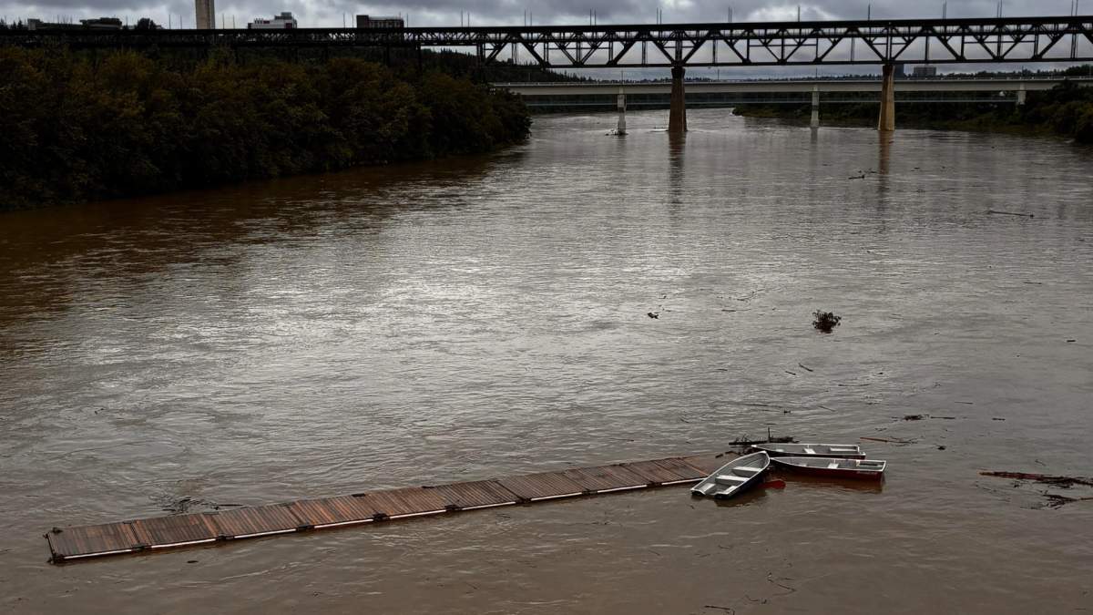 A dock with five boats attached is seen floating down the North Saskatchewan River in Edmonton, Alta., on June 22, 2026.